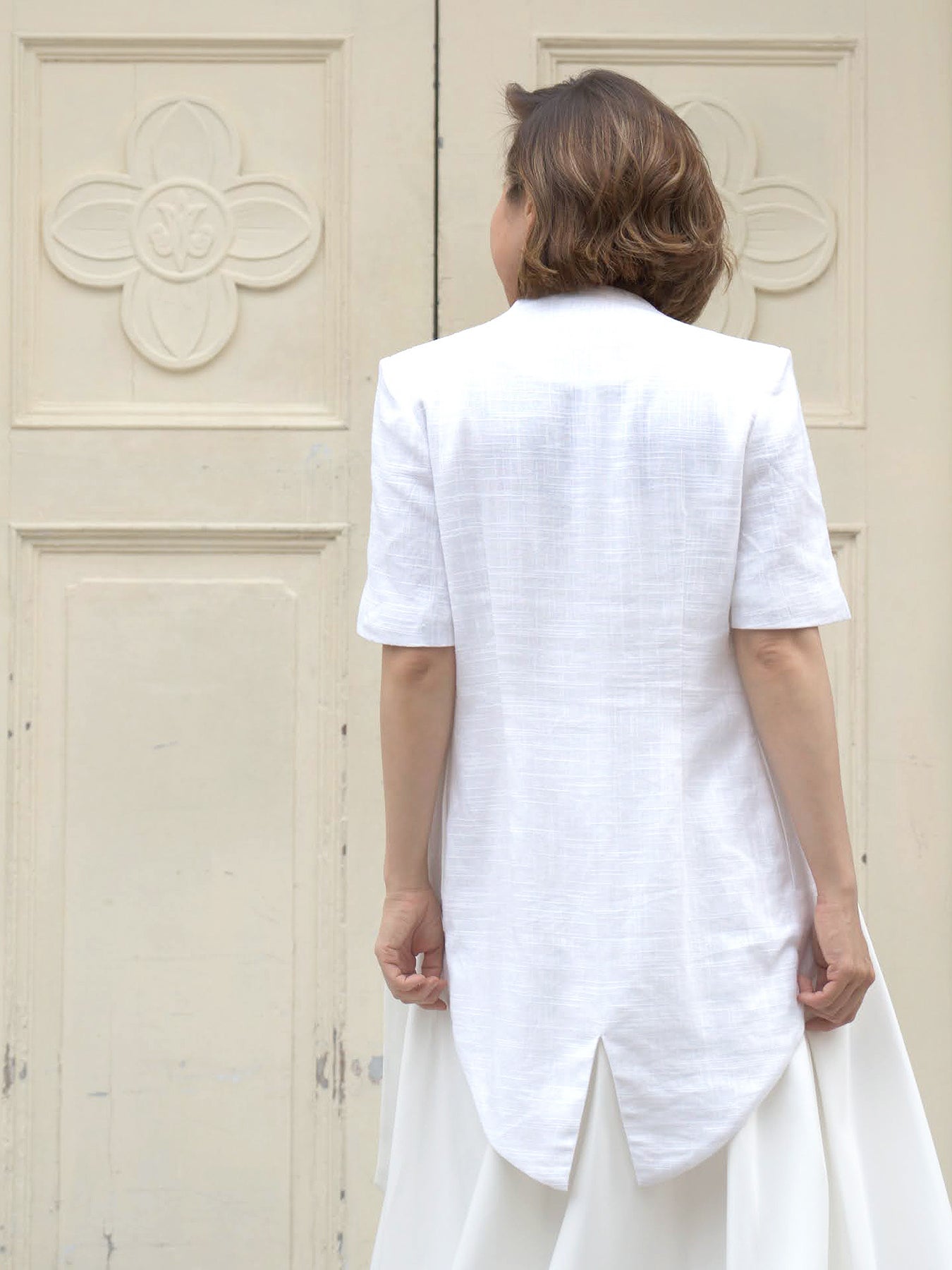 Woman wearing a white outerwear jacket with tailcoat and white skirt by Singapore fashion brand Hadasity.