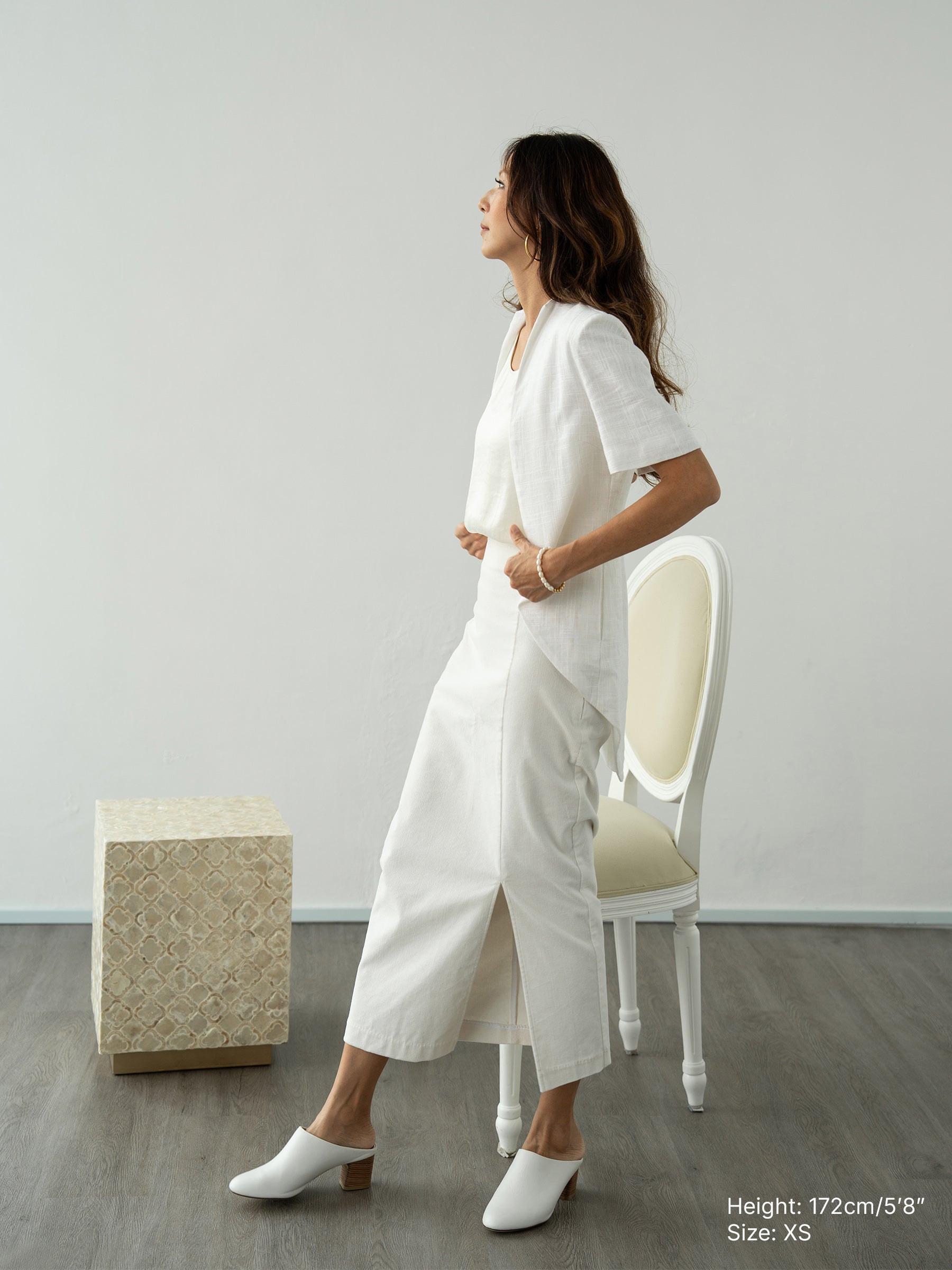 Woman wearing a white outerwear jacket with tailcoat and white corduroy skirt by Singapore fashion brand Hadasity.