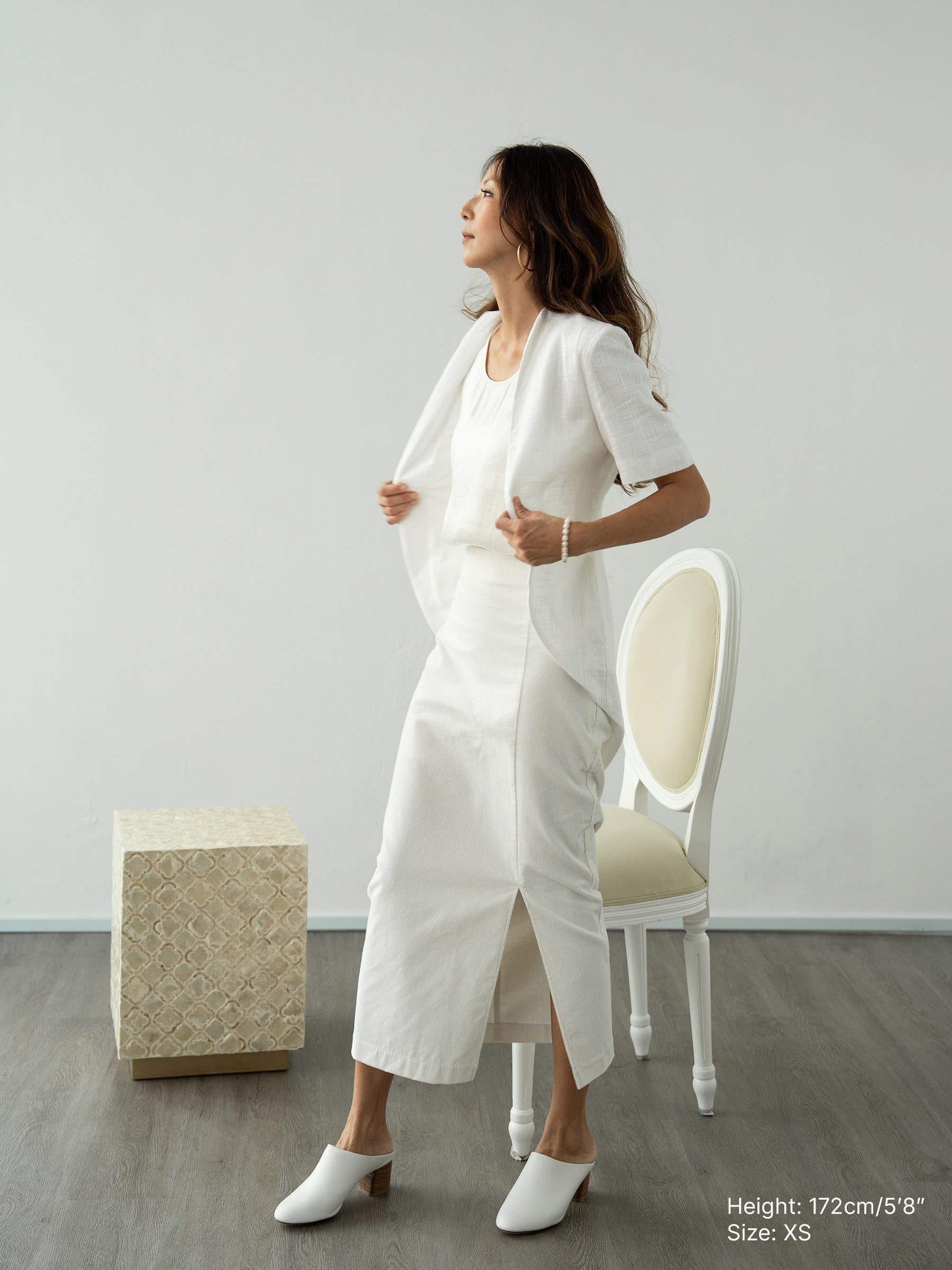 Woman wearing a white outerwear jacket with tailcoat and white corduroy skirt by Singapore fashion brand Hadasity.