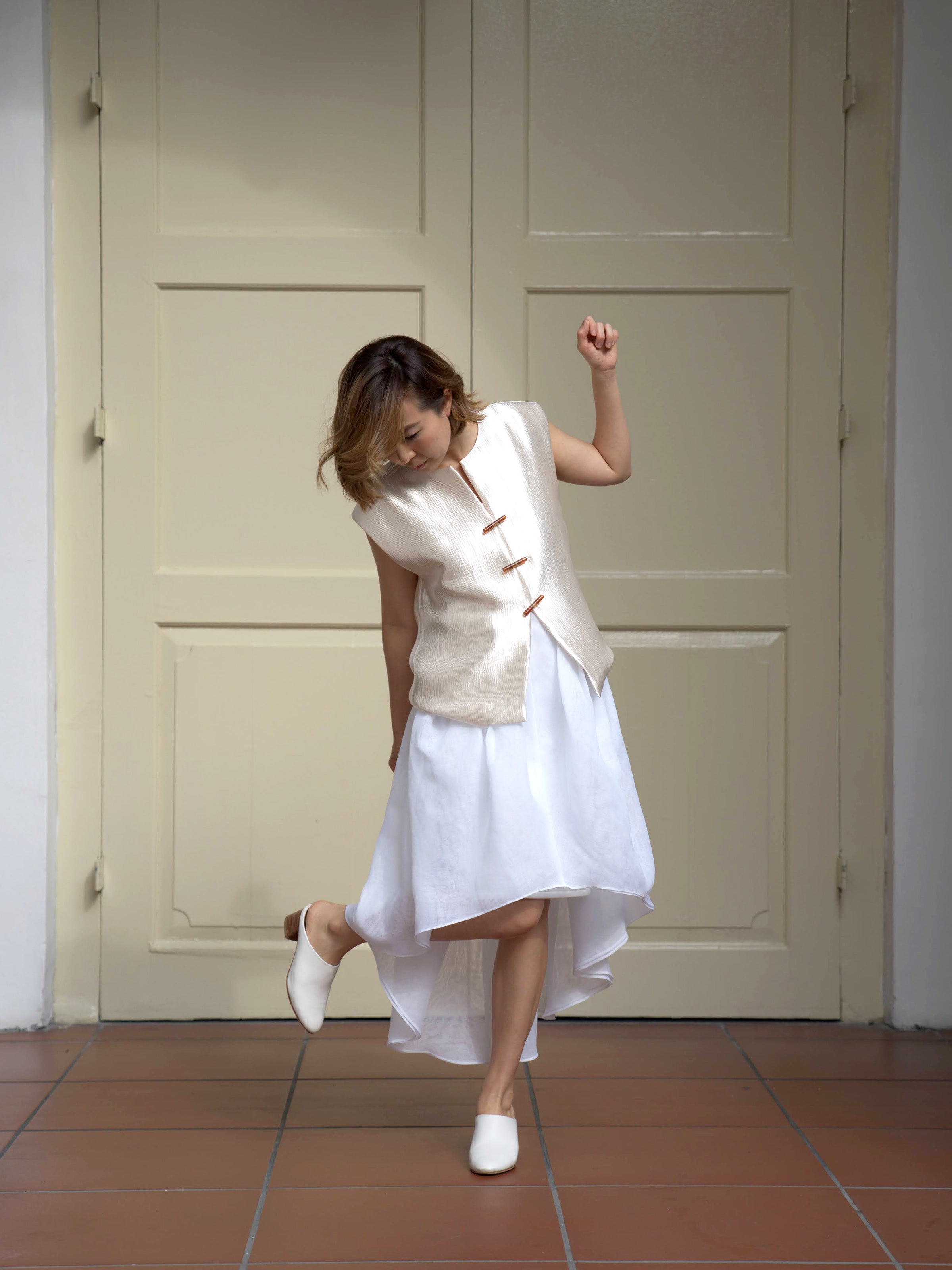 Woman wearing white asymmetrical designer skirt and gold shimmer sleeveless vest by Singapore women's fashion brand Hadasity.