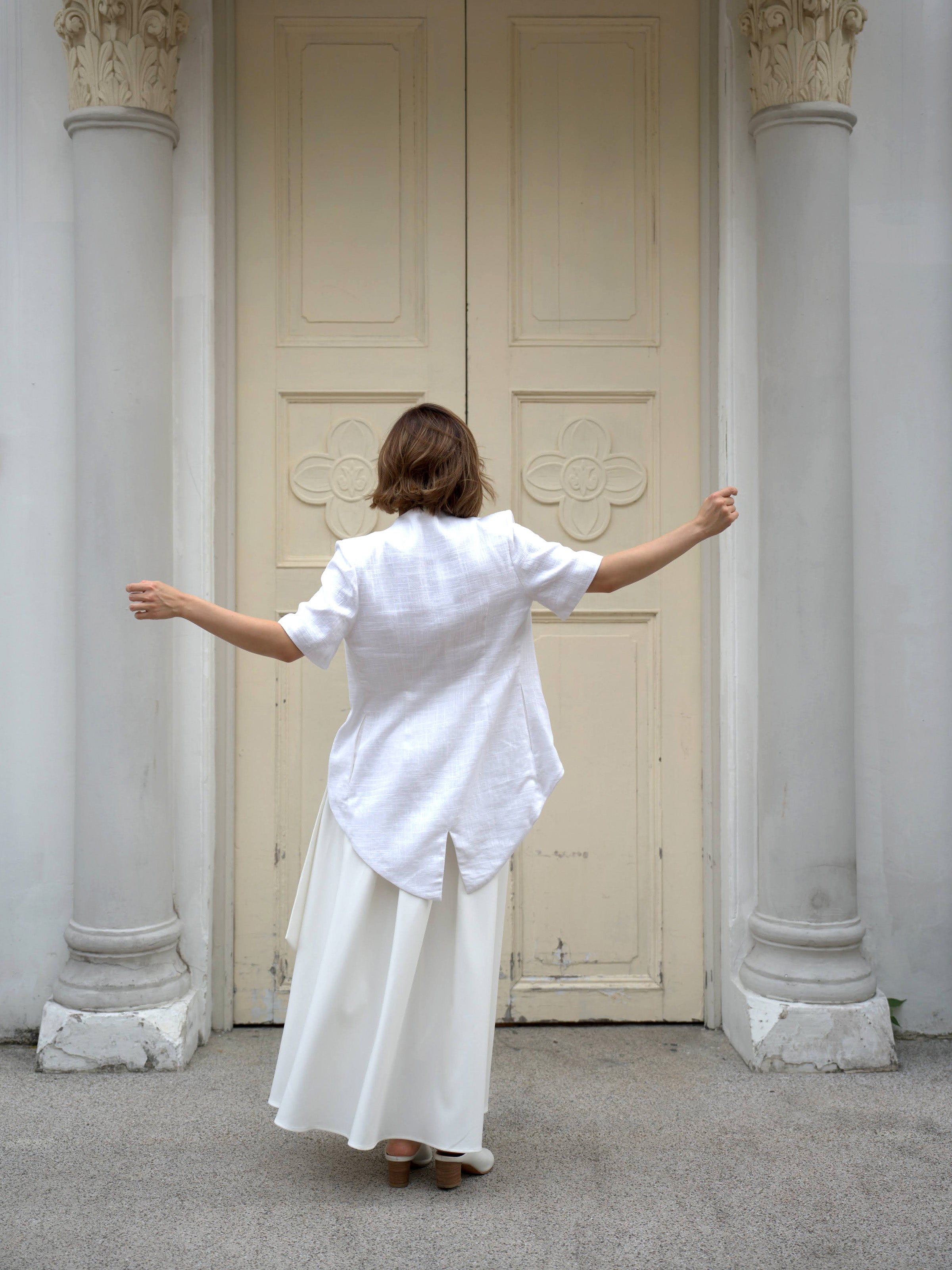 Woman wearing a white outerwear jacket with tailcoat and white skirt by Singapore fashion brand Hadasity. 