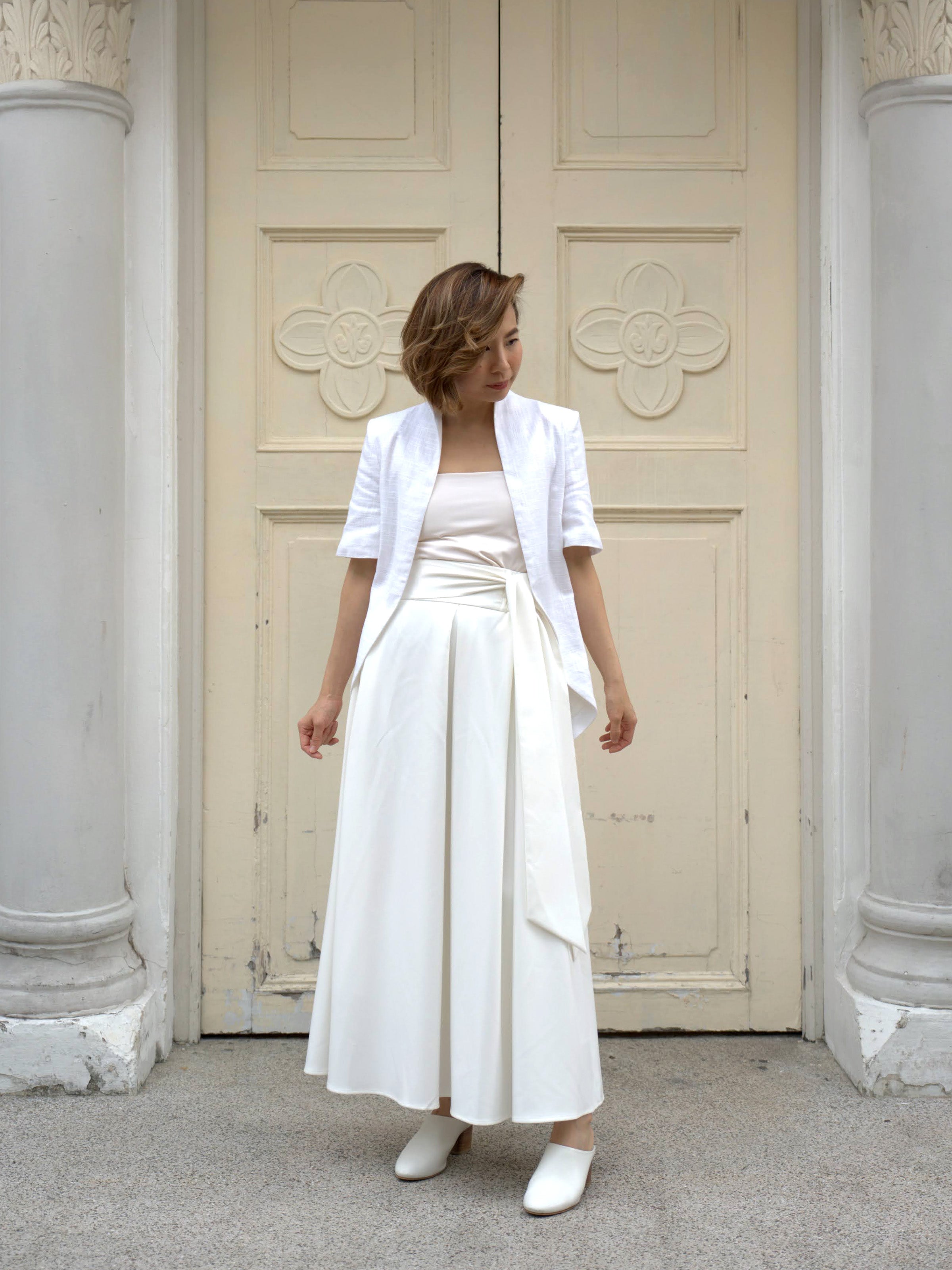 Woman wearing a white outerwear jacket with tailcoat and white skirt by Singapore fashion brand Hadasity.