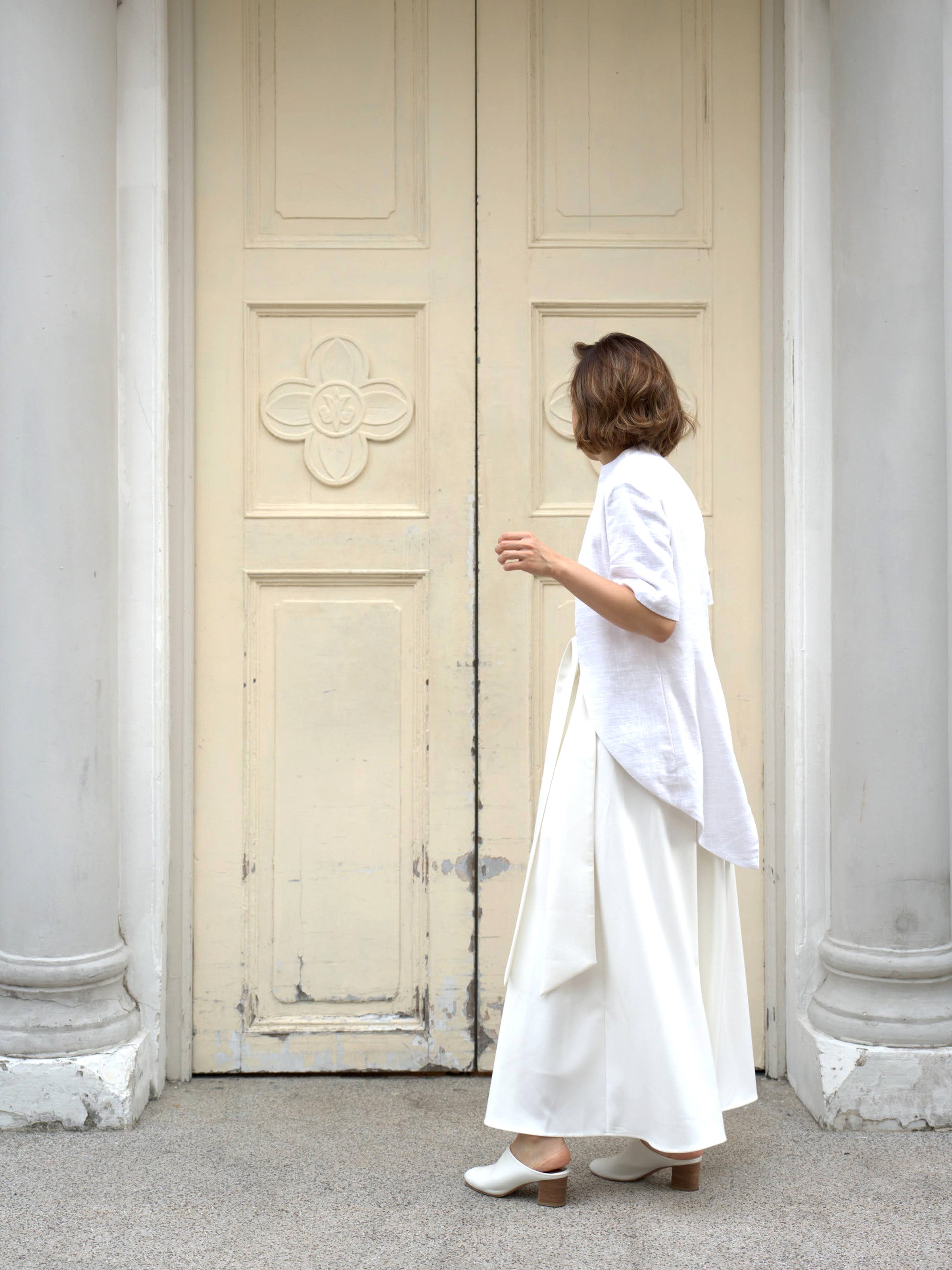 Woman wearing a white outerwear jacket with tailcoat and white skirt by Singapore fashion brand Hadasity.