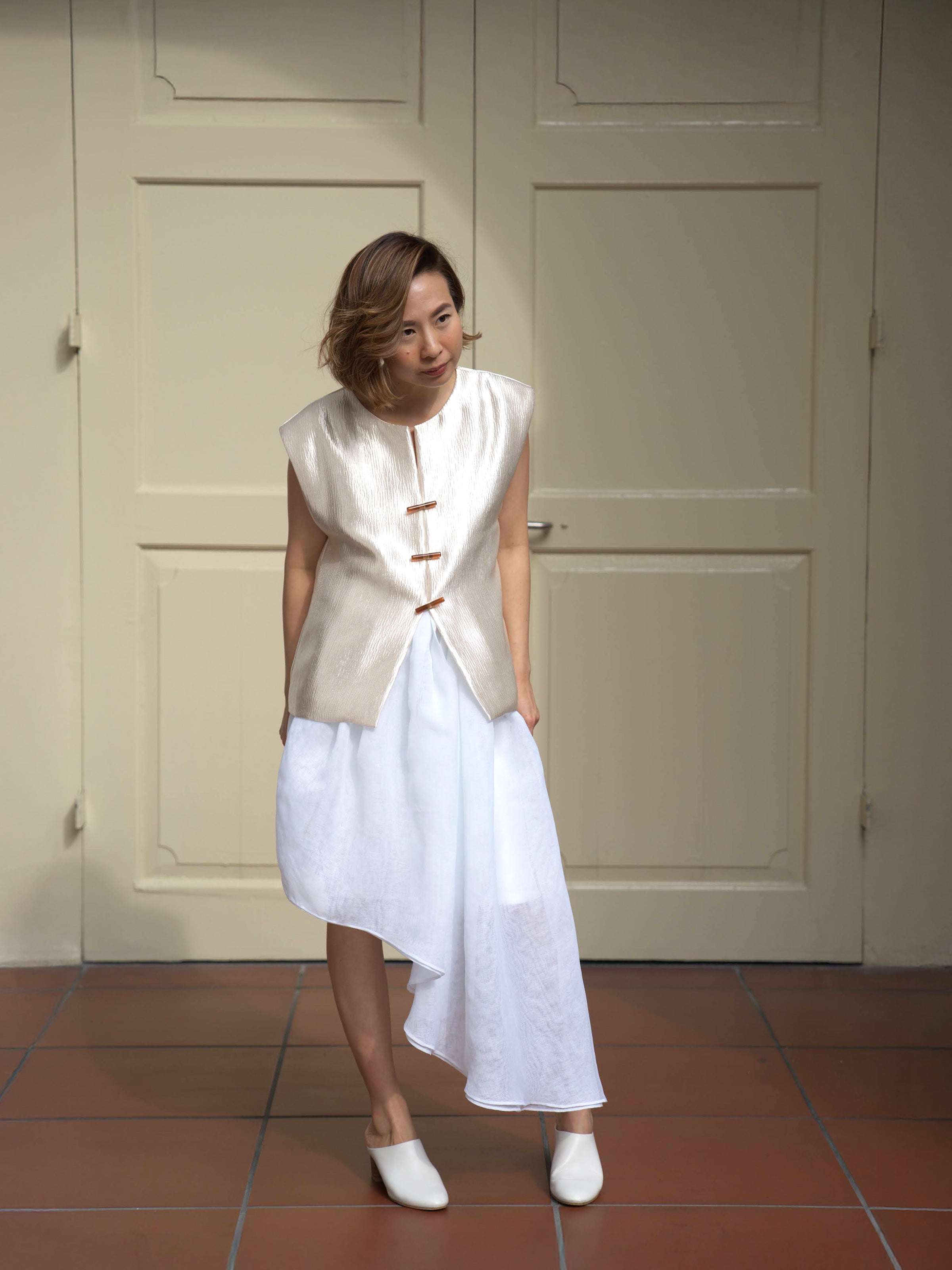 Woman wearing white asymmetrical designer skirt and gold shimmer sleeveless vest by Singapore women's fashion brand Hadasity.